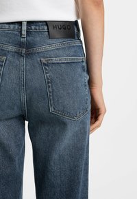 Donkerblauwe denim jeans met een rechte pasvorm, voorzien van achterzakken en een zwart leren logo-label met de tekst "HUGO" op de tailleband.