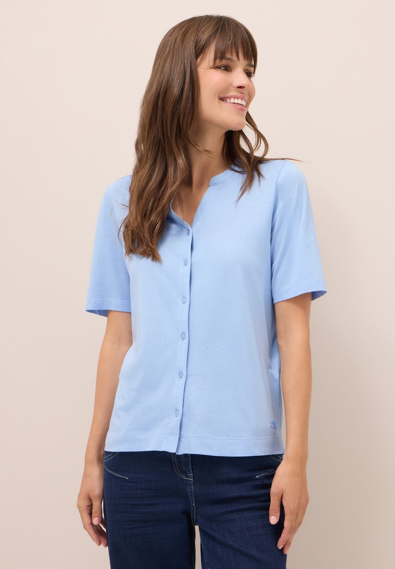 Himmelblaues kurzärmliges Hemd mit Knöpfen aus weicher Baumwolle, featuring einen runden Halsausschnitt und eine lockere Passform, kombiniert mit dunkelblauen Jeans.