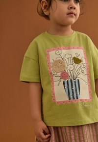 T-shirt di cotone verde con stampa grafica floreale, con dettagli di tessuto testurizzato e bordo scallopato rosa.