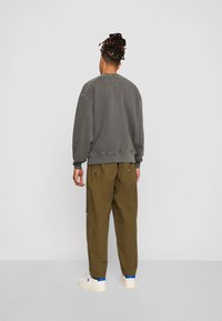 Felpa grigia in cotone con orlo e polsini a costine, abbinata a pantaloni cargo verde oliva con tasche laterali e cuciture a vista, indossata con sneaker bianche.
