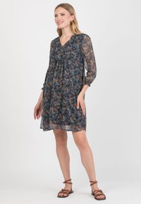 Luźna, kwiatowa sukienka w odcieniu granatowym z długimi, przezroczystymi rękawami i dekoltem w kształcie litery V. Posiada marszczoną górę i lekką, przezroczystą teksturę.