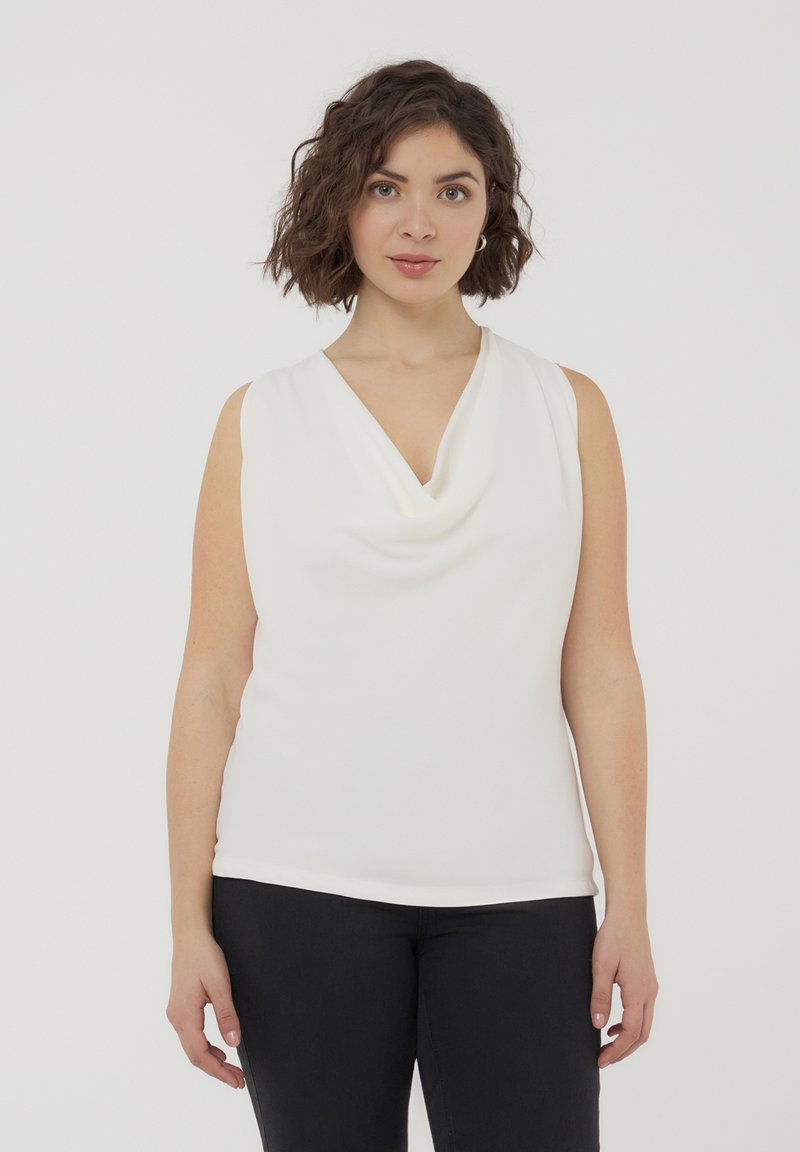 Top bianco senza maniche con scollo drappeggiato, texture liscia e design aderente. Abbinato a pantaloni neri, creando un semplice look bicolore.
