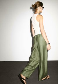 Groene linnen culotte met een gestructureerde afwerking en een elastische tailleband, gecombineerd met een grijs tanktop en zwarte sandalen.
