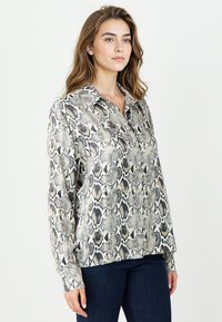 Bluzka z długim rękawem w beżowy i czarny wzór węża. Posiada kołnierzyk oraz luźny krój. Gładka tekstura i lekki materiał.