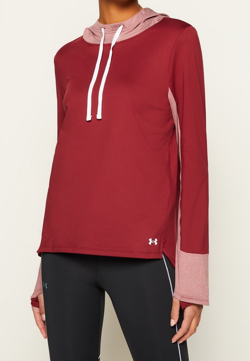 Femme portant un haut de sport à capuche bordeaux à manches longues avec des trous pour les pouces et des leggings noirs avec un liseré blanc.