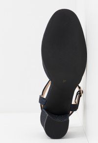 Mörkblå högklackad sandal med texturerad ovandel, justerbar rem runt vristen och svart gummisula. Storlek 37 märkta på sulan.