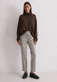 Brązowy sweter z golfem w luźnym kroju, zestawiony z jasnoszarymi spodniami o teksturowanej fakturze i czarnymi mokasynami. Prosty, nowoczesny i minimalistyczny design.