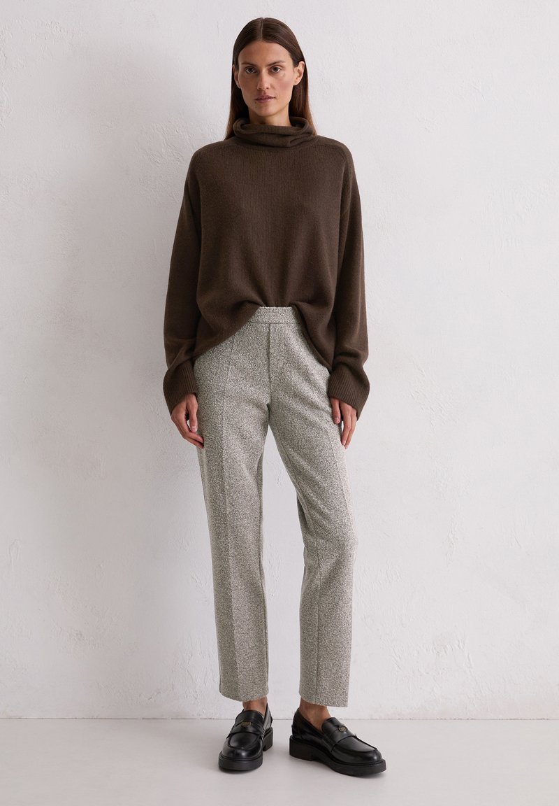 Brązowy sweter z golfem w luźnym kroju, zestawiony z jasnoszarymi spodniami o teksturowanej fakturze i czarnymi mokasynami. Prosty, nowoczesny i minimalistyczny design.