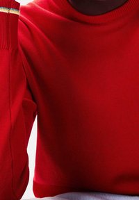 Rød strikket sweater med rund hals og langeærmer, med en stribet detalje i blå og gul ved manchetterne. Blød tekstur.