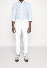 Ljusblå randig skjorta med uppvikta ärmar, vita slim-fit byxor och grå sneakers med blå detaljer. Avslappnad, modern design.