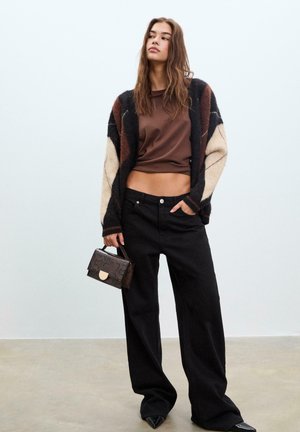 Top court marron associé à un cardigan tricot multicolore. Un pantalon à jambes larges noir et un petit sac à main à motifs sont inclus.