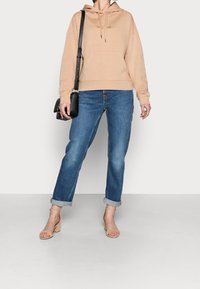 Beige hoodie med känguruficka, parat med ljusblå jeans med uppvikta ben och nude blockklackssandaler, kompletterat med en svart axelremsväska.