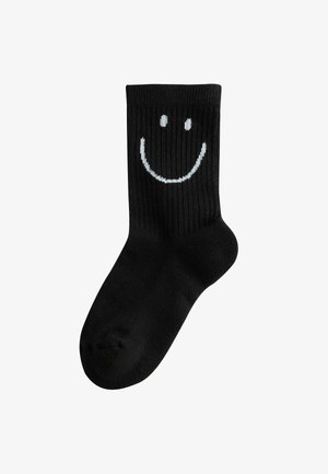 Calzini neri a crew con texture a coste, caratterizzati da un design di faccina sorridente bianca sulla parte superiore del polpaccio.