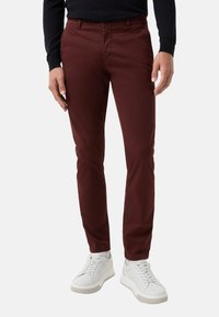 Burgunderfarbene Chinos aus Baumwolle mit schlankem Schnitt. Kombiniert mit weißen Sneakers, die eine glatte Textur und ein minimalistisches Design aufweisen.