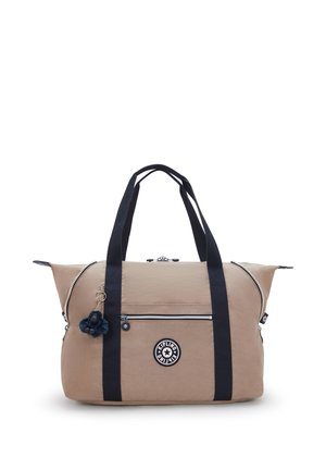 Beige fabric duffel bag with navy handles, zippered closures, front pocket, and a dark blue pom-pom charm. Features a logo patch.
