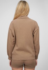 Camicia marrone a trama con vestibilità rilassata e maniche lunghe, abbinata a pantaloni corti marroni dello stesso colore. Il tessuto presenta un leggero motivo trapuntato.