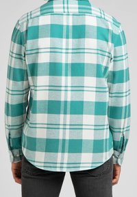 Chemise en flanelle à carreaux turquoise et blanche, manches longues, poignets à boutons, ourlet arrondi et finition douce et texturée.