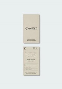 Deux étiquettes beige promouvant la mode durable : à l’avant, il est écrit "Committed" et "Making fashion more sustainable,", au dos, détails sur la réduction des produits chimiques, de l'eau et de l'énergie.