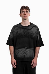 Černé oversize tričko s bledým vzorem a vystouplým logem „FAVELAS WORLDWIDE“ uprostřed. Materiál bavlna, krátké rukávy, kulatý výstřih.