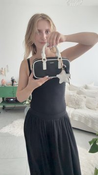 Donna in abito nero che tiene una piccola borsa bianca e nera con portachiavi a forma di stella in un soggiorno moderno e luminoso.