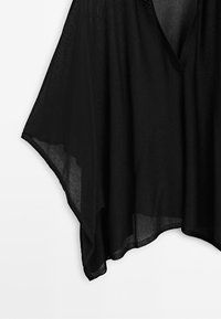 Black sheer fabric with a V-neckline and asymmetrical hem, hanging against a white background.