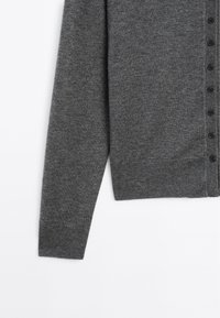 Cardigan gris en tissu tricoté doux, avec des manches longues, un devant à boutons avec six boutons foncés et un ourlet côtelé.