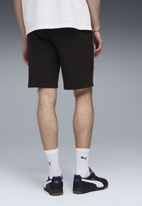 Svarta bomullsshorts med rak skärning och vita sidostråk, bärs med vita strumpor och svarta sportskor med lila detaljer.