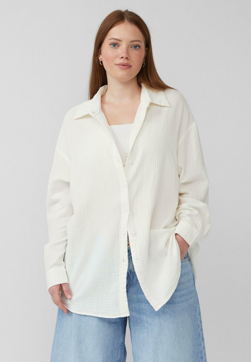 Witte button-up shirt van een gestructureerde stof, met een kraag en een oversized pasvorm. Gepaard met lichtblauwe brede jeans.
