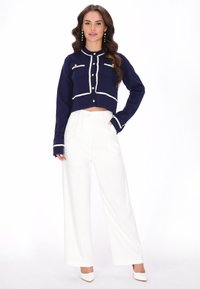 Námořnická zkrácená bunda s bílým lemem a knoflíky, se dvěma předními kapsami. V kombinaci s bílými širokými kalhotami s vysokým pasem a podpatky.