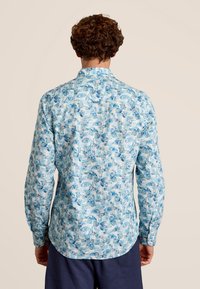 Lichtblauw overhemdd met een patroon van tropische bladeren en strepen. Lange mouwen en een klassieke kraag.