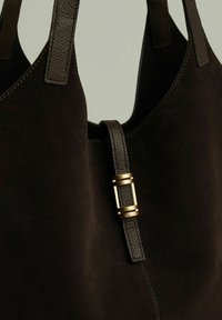 Czarna zamszowa torba na ramię ze gładkimi skórzanymi uchwytami i złotym metalowym akcentem. Posiada przestronną komorę i minimalistyczny design.