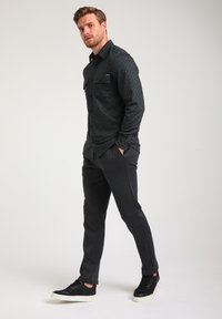 Zwarte button-up shirt met geometrisch patroon, gecombineerd met gestructureerde donkere broeken en zwarte sneakers met witte zolen; aansluitend ontwerp, lange mouwen.