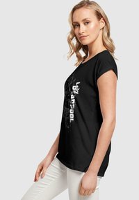 Sort bomulds t-shirt med en afslappet pasform, der viser et grafisk print af "Lady Deadpool" i hvid. Raglanærmer, blød tekstur.