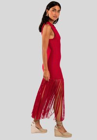 Vestido de punto rojo con detalle de flecos en el dobladillo, diseño sin mangas y silueta ajustada. Combinado con sandalias de cuña beiges.