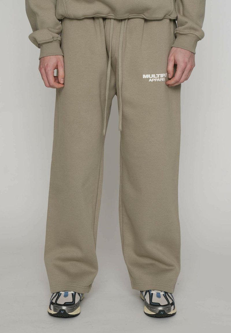 Beige Jogginghose mit einem Tunnelzug in der Taille, gerippten Bündchen und einem weißen Logo am linken Oberschenkel. Das Material wirkt weich und strukturiert.