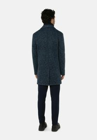 Wollen overcoat in donkerblauw met een gestructureerde afwerking, voorzien van een enkele split aan de achterkant en een klassiek kraagontwerp. Draag het met een marineblauwe broek.