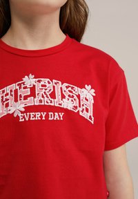 Piros pamut póló, fehér hímzett "CHERISH" felirattal, virágos részletekkel és alatta a "EVERY DAY" szöveggel. Klasszikus crew neck kialakítás.