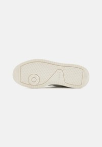 Levi's vászoncipő talpa krém színű gumiból készült, texturált mintával, körkörös díszítéssel és bordázott szélekkel a tapadás érdekében. Minimalista dizájn, világos szín.
