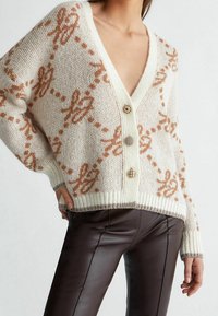 Cardigan de punto en crema con un patrón floral en marrón claro, con un escote en V profundo, tres botones y puños y dobladillo acanalados.