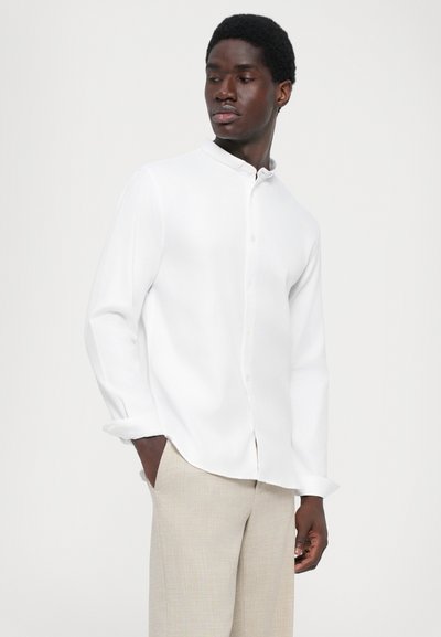 Witte long-sleeve shirt met een staande kraag, gemaakt van zachte stof, met een knoopsluiting aan de voorkant en opgerolde manchetten. Gecombineerd met lichtgekleurde broek.