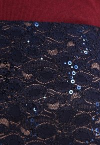 Spetsklänning med en mörk marinblå, paljetterad nederdel och en bordeauxfärgad, ribbad överdel som visar upp intrikata mönster och texturer.