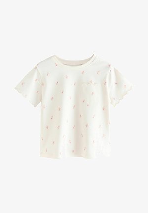 Balta īsām piedurknēm T-kreklā ar viļņotu malu, kurā ir izkaisīti rozā ziedu raksti un neliela viļņota kabata kreisajā pusē.