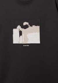 Schwarzer Sweatshirt mit einem rechteckigen, bestickten Patch in Beige, der abstrakte Linien und Formen zeigt. Darunter steht der Text "Eine neue Idee."