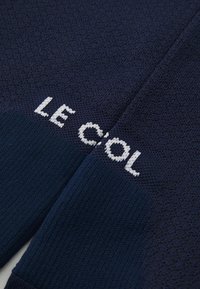 Tejido de punto azul marino con textura acanalada, que presenta el texto blanco "LE COL" destacado en un lado.