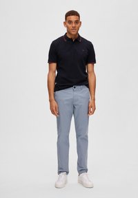 Jūras spēku polo krekls ar sarkaniem apkakles akcentiem, apvienots ar gaiši pelēkiem biksēm un baltām sporta apaviem. Slim fit, īsām piedurknēm, ikdienišķs dizains.
