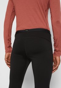 Black leggings with a wide waistband, featuring an elastic band and stitching details, paired with a long-sleeve, maroon shirt.