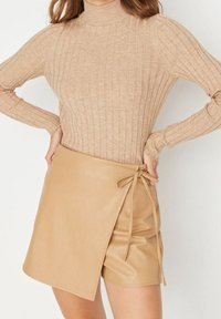 Beżowy sweter z golfem i prążkowanym wzorem w zestawie z brązową spódnicą z imitacji skóry z bocznym wiązaniem i gładką fakturą.