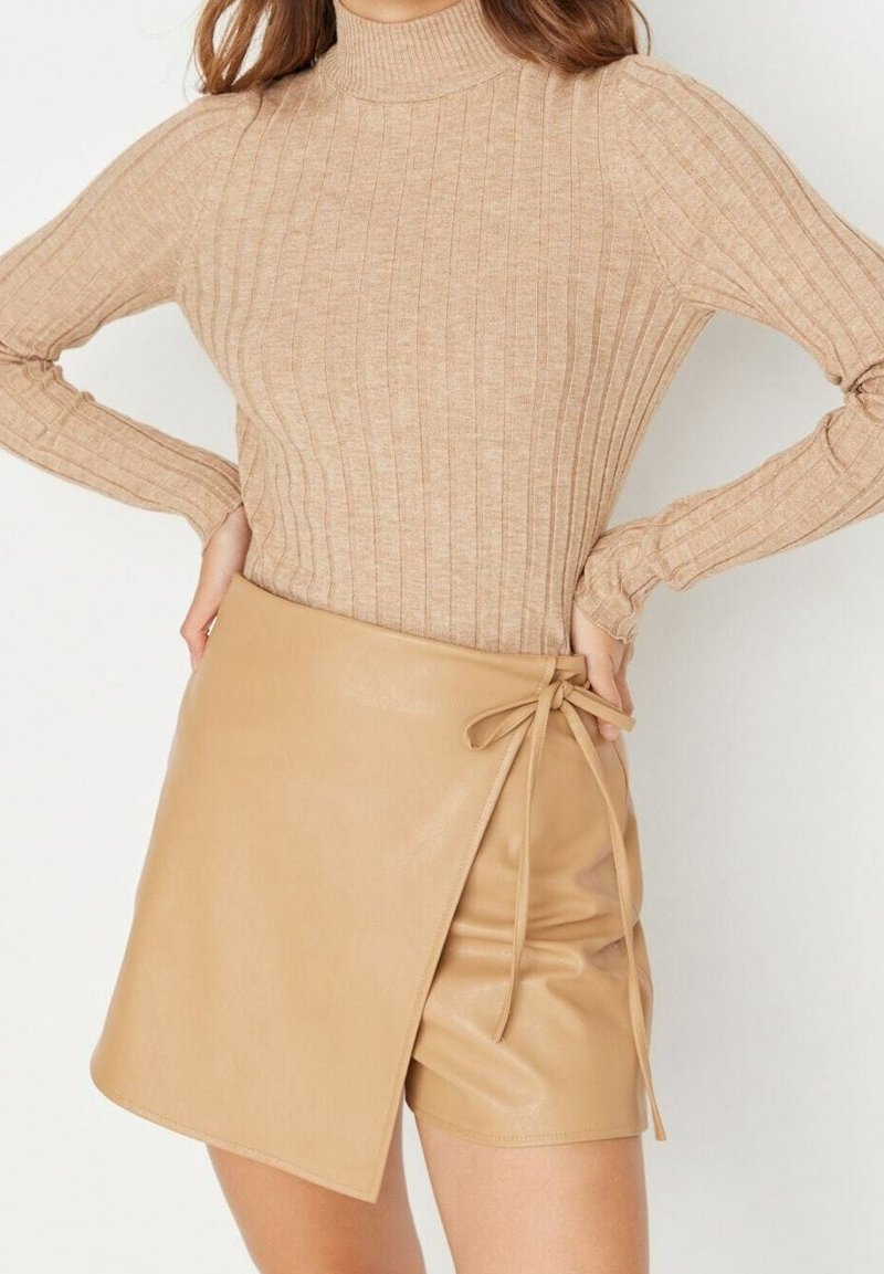 Beżowy sweter z golfem i prążkowanym wzorem w zestawie z brązową spódnicą z imitacji skóry z bocznym wiązaniem i gładką fakturą.