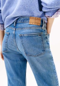 Jeans in denim azzurro chiaro con vita alta, dotati di tasche posteriori e una toppa in pelle color cuoio con la scritta "TOMMY JEANS" in rilievo. Tessuto dalla trama visibile.