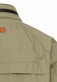 Veste vert olive claire, en tissu lisse, avec un col zippé et une étiquette en cuir à l'arrière.